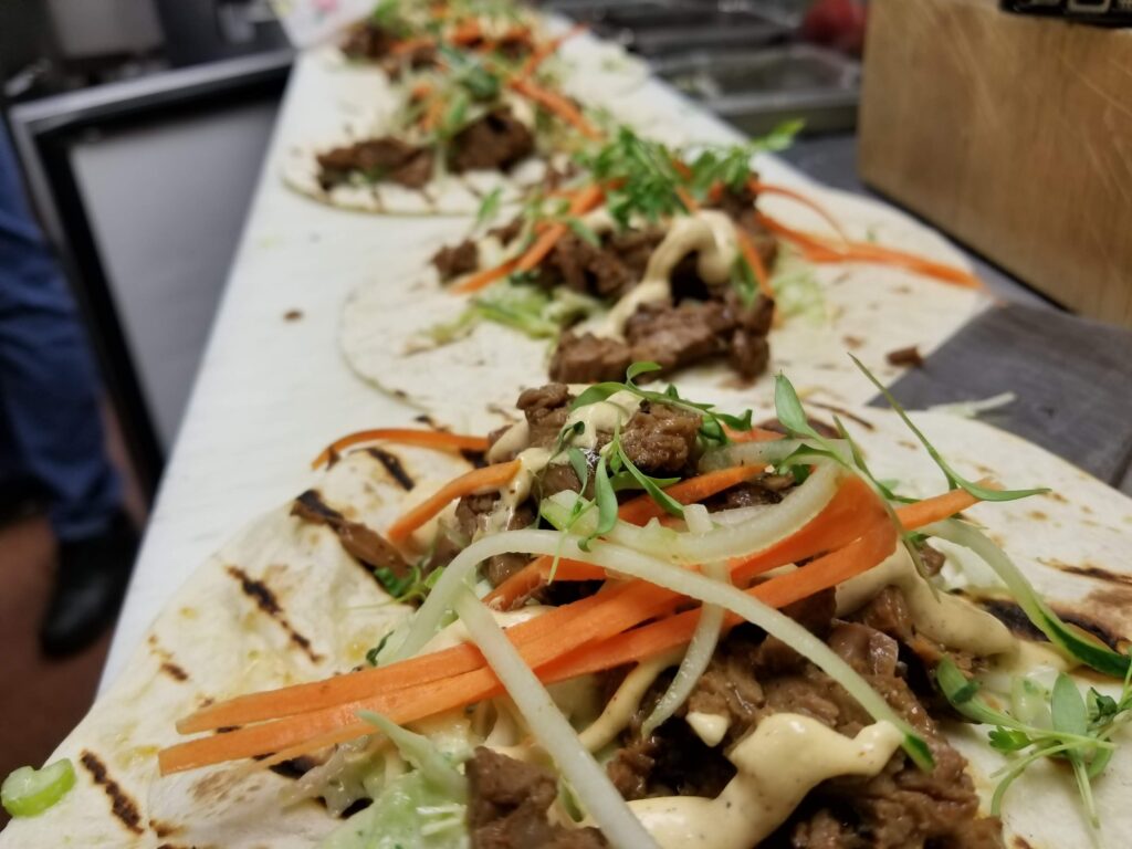 Closeup of grilled meat tacos with carrots and greens.