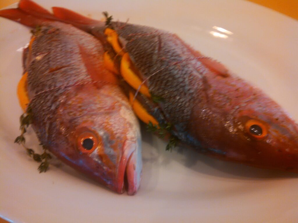 Two fish are sitting on a plate with some herbs.