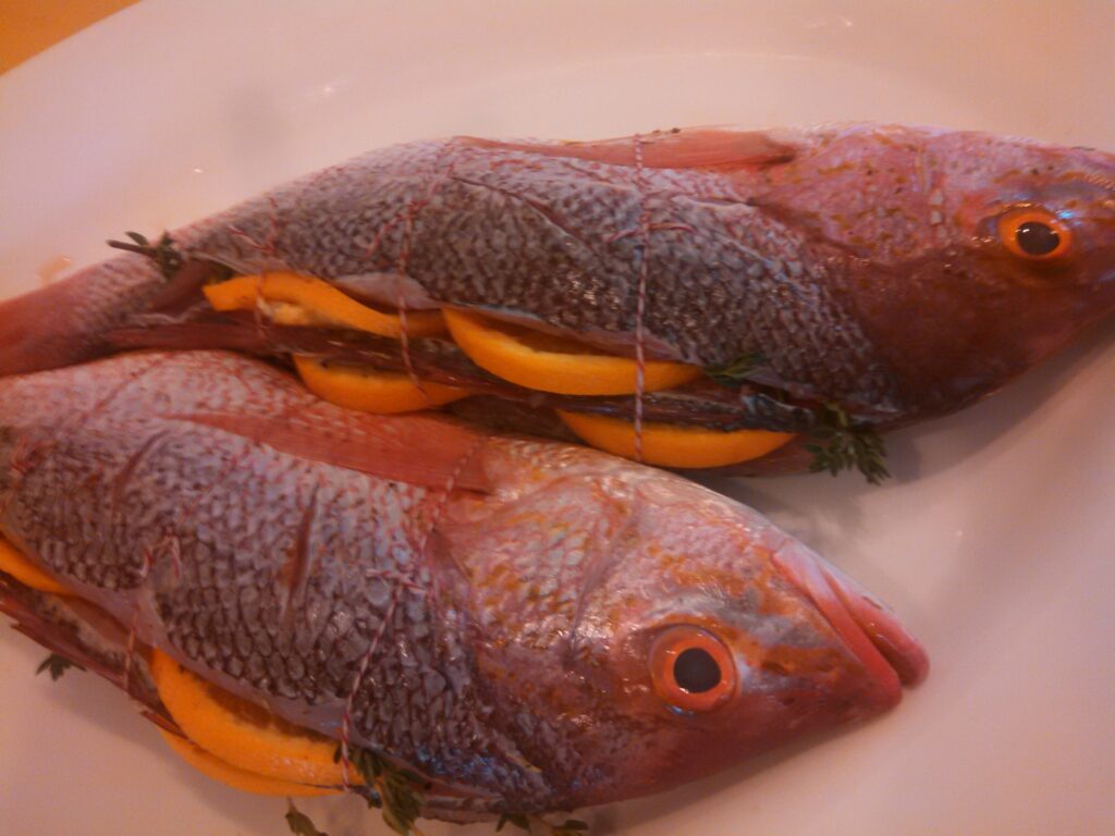 Two fish are sitting on a plate with some orange slices.