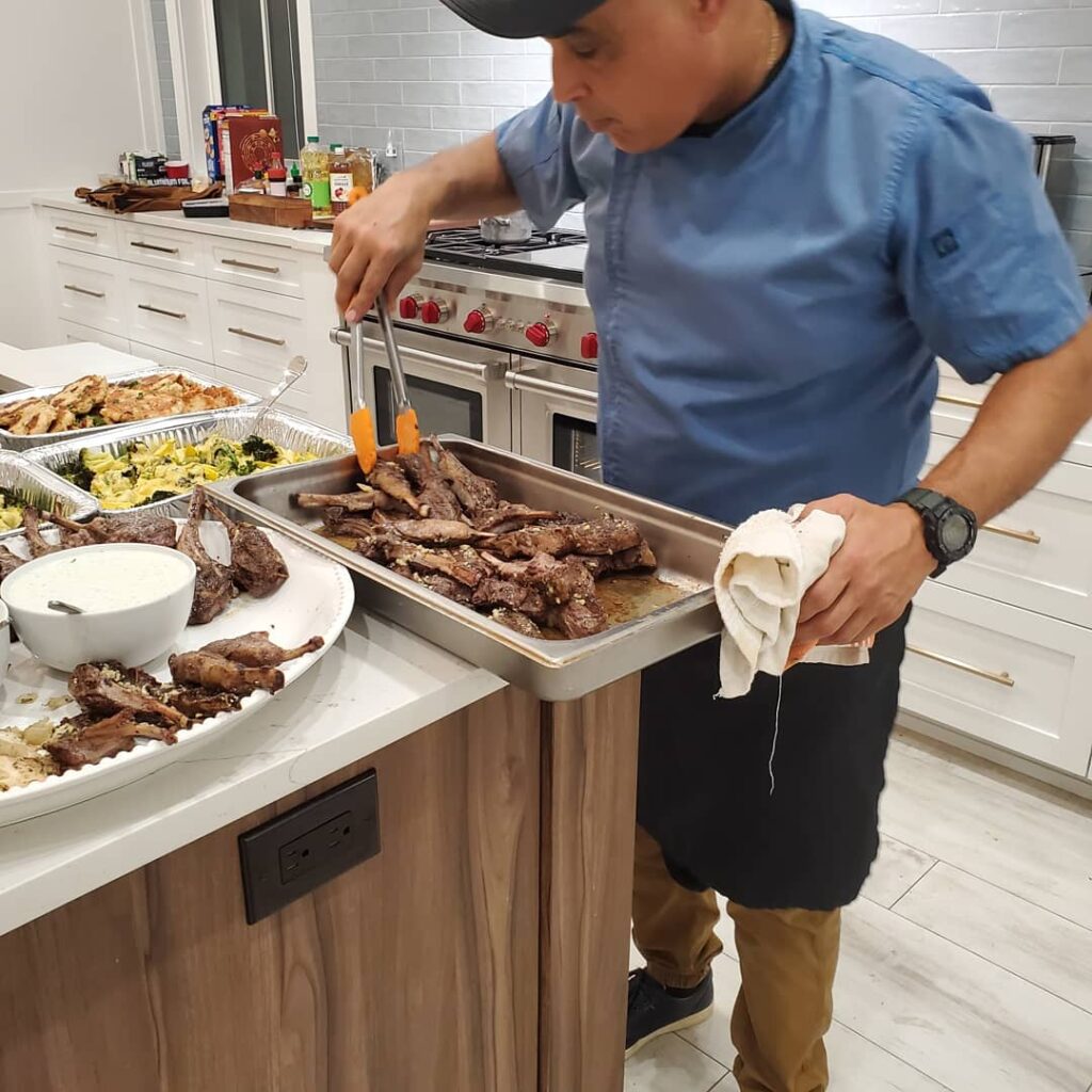 A man in blue shirt and black hat standing next to food.